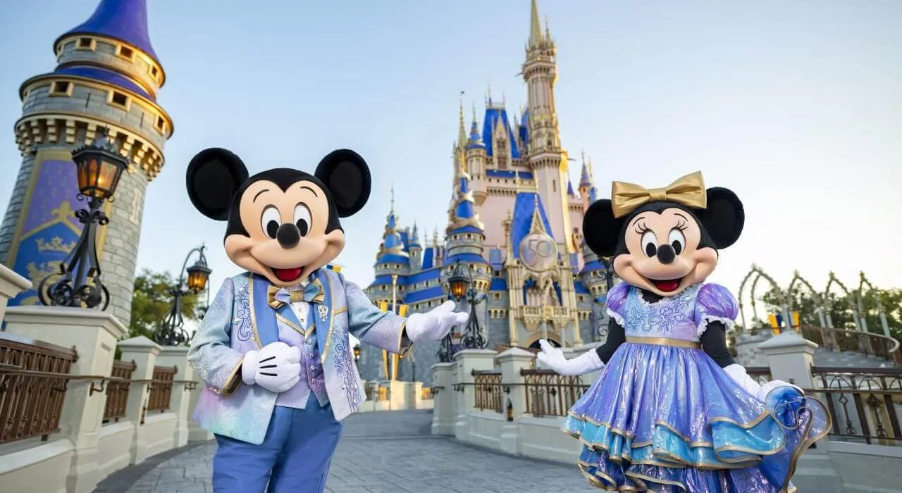 Mickey Mouse y Minnie Mouse con atuendos festivos y brillantes posando con orgullo frente al Castillo de Cenicienta en Magic Kingdom, Orlando, destacando servicios completos de viaje Disney.